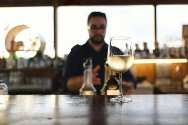 Glas Wein auf dem Tisch mit Barkeeper im Hintergrund in einem Cafe - ASGF04524