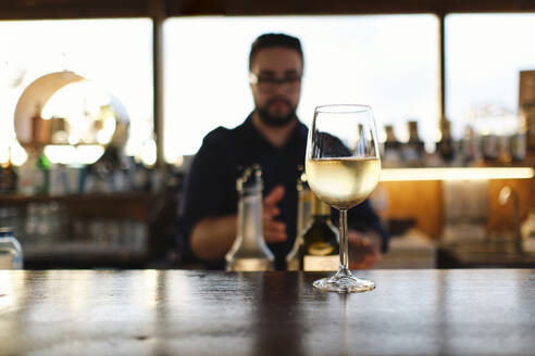 Glass of wine on table with bartender in background at cafe - ASGF04524