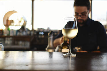 Glas Weißwein auf dem Tisch mit Barkeeper im Hintergrund - ASGF04525