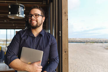 Happy young engineer standing with laptop - ASGF04529