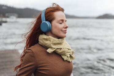 Redhead woman with eyes closed listening to music through wireless headphones - KNSF09746