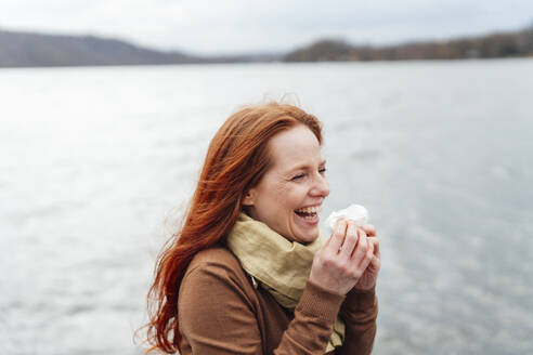 Rothaarige Frau hält Seidenpapier und lacht am See - KNSF09754