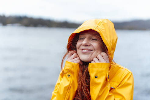 Smiling woman with eyes closed wearing hood of jacket - KNSF09764