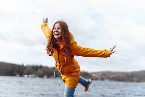Carefree woman with arms outstretched in front of lake - KNSF09768
