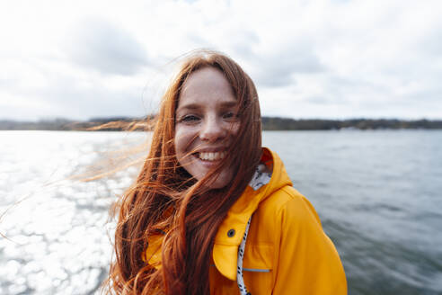 Smiling redhead woman with long hair in front of lake - KNSF09771