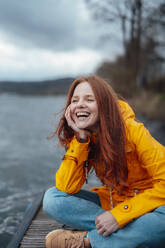 Happy woman sitting cross-legged on pier - KNSF09776