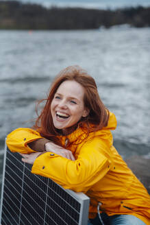 Fröhliche Frau lehnt an einem Sonnenkollektor am See - KNSF09781
