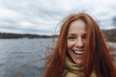 Redhead woman with long hair laughing in front of lake - KNSF09794