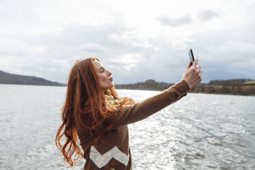 Redhead woman taking selfie over smart phone by lake - KNSF09806