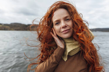 Redhead woman with long hair in front of lake and cloudy sky - KNSF09813