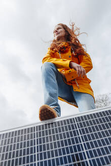 Redhead woman with leg on solar panel in front of sky - KNSF09819