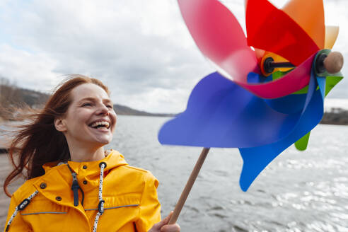 Cheerful woman with pinwheel toy by lake - KNSF09820