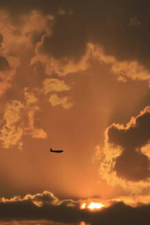 Silhouette of commercial airplane flying against moody sky at sunset - JTF02369