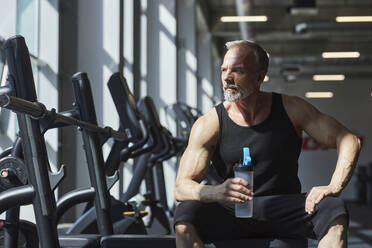 Nachdenklicher reifer Mann mit Wasserflasche im Fitnessstudio - KPEF00196