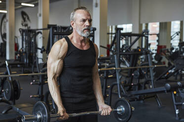 Selbstbewusster reifer Mann beim Training mit der Langhantel im Fitnessstudio - KPEF00217