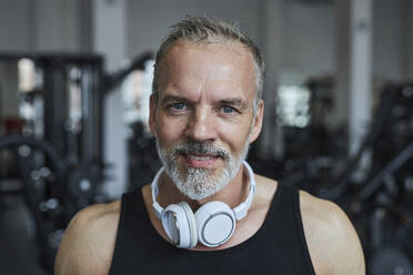 Lächelnder reifer Mann mit Kopfhörern im Fitnessstudio - KPEF00227