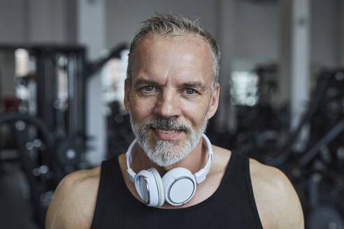 Smiling mature man with headphones in health club - KPEF00227