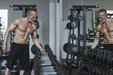 Hemdloser Mann wählt Hantel in der Nähe von Spiegel im Fitnessstudio angeordnet - KPEF00237