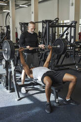 Älterer Trainer hilft Mann beim Krafttraining im Fitnessstudio - KPEF00245
