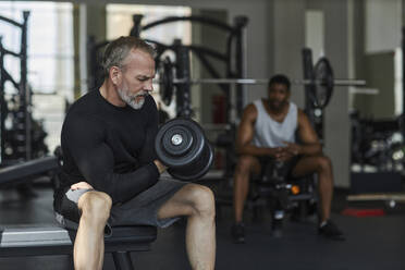 Älterer Mann trainiert mit Mann im Hintergrund im Fitnessstudio - KPEF00246