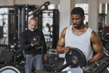 Junger Mann, der eine Langhantel im Fitnessstudio mit Gewicht belastet - KPEF00247