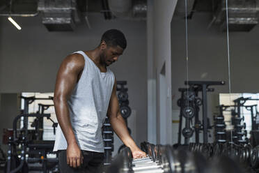 Young man choosing dumbbell in gym - KPEF00249