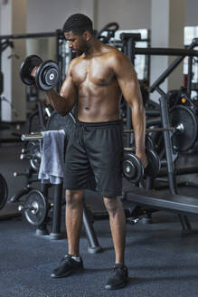 Shirtless man exercising with dumbbells in health club - KPEF00256