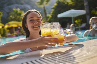 Glückliche Frau mit einem Glas Orangensaft im Pool an einem sonnigen Tag - ANNF00447