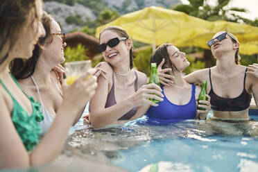 Carefree friends holding beer bottles and enjoying in pool - ANNF00466