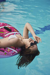 Teenager-Mädchen mit Sonnenbrille auf einem Schwimmschlauch im Pool liegend - ANNF00473