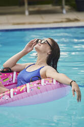 Teenage girl wearing sunglasses relaxing with inflatable swimming ring in pool - ANNF00474