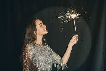 Smiling woman holding sparkler in front of black curtain - ADF00155