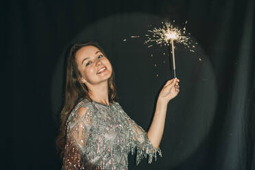 Happy woman holding sparkler in front of black curtain - ADF00156