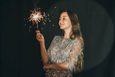 Smiling woman looking at sparkler in front of black curtain - ADF00157