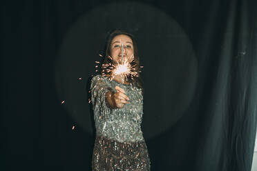 Young woman holding sparkler in front of black curtain - ADF00158