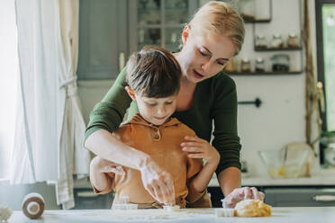 Mutter und Sohn schneiden Teig mit Ausstechformen in der Küche aus - VSNF01333
