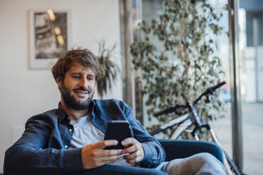 Lächelnder Geschäftsmann, der ein Smartphone im Büro benutzt - JOSEF20555