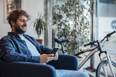 Glücklicher Geschäftsmann mit Smartphone im Büro - JOSEF20556