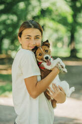 Teenage girl holding dog in park - VSNF01341