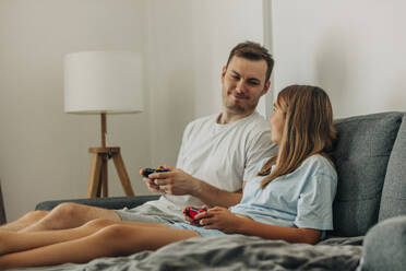 Smiling bother and sister playing video game on bed at home - VSNF01344