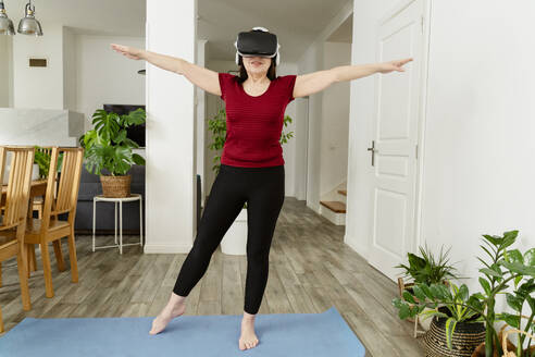 Active woman with arms outstretched wearing VR glasses at home - OSF02059