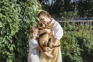 Mutter und Sohn umarmen Hund im Hinterhof an einem sonnigen Tag - VBUF00339