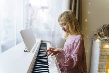 Blond girl playing piano at home on Christmas - NJAF00573