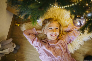 Lächelndes Mädchen unter dem Weihnachtsbaum zu Hause liegend - NJAF00579