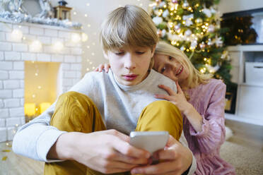 Junge benutzt Smartphone mit Schwester zu Hause an Weihnachten - NJAF00583