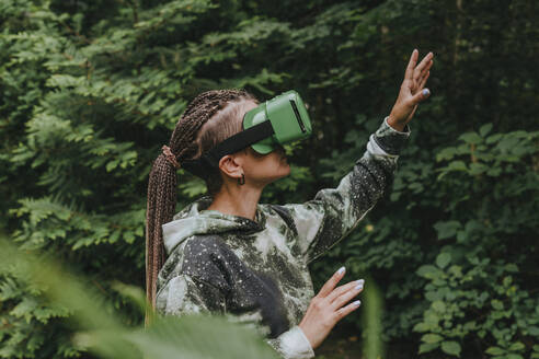 Frau gestikuliert und schaut durch eine futuristische Brille auf einen Wald - YTF01094