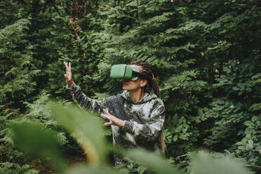 Frau gestikuliert und erkundet Bäume durch ein VR-Headset - YTF01096
