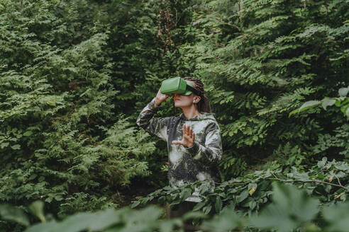 Frau mit VR-Brille beobachtet Bäume im Wald - YTF01097