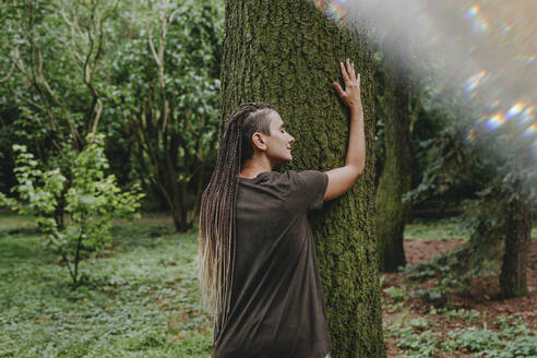 Frau mit geflochtenem Haar umarmt Baum im Wald - YTF01118