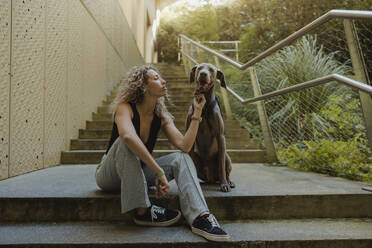 Young woman stroking dog sitting on steps - MTBF01272